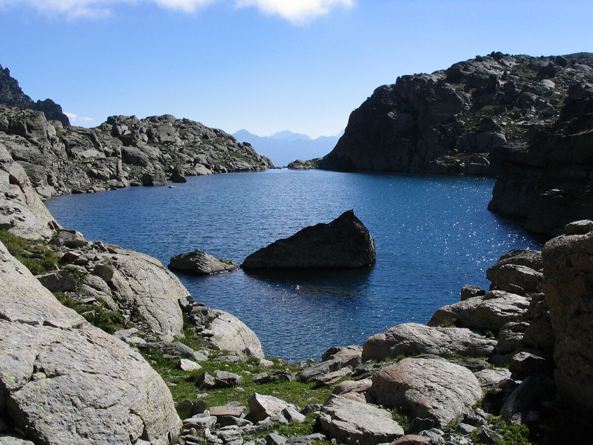 caratteristico lago alpino con acqua di colore blu intenso, in mezzo al lago si erge una grande roccia a forma triangolare