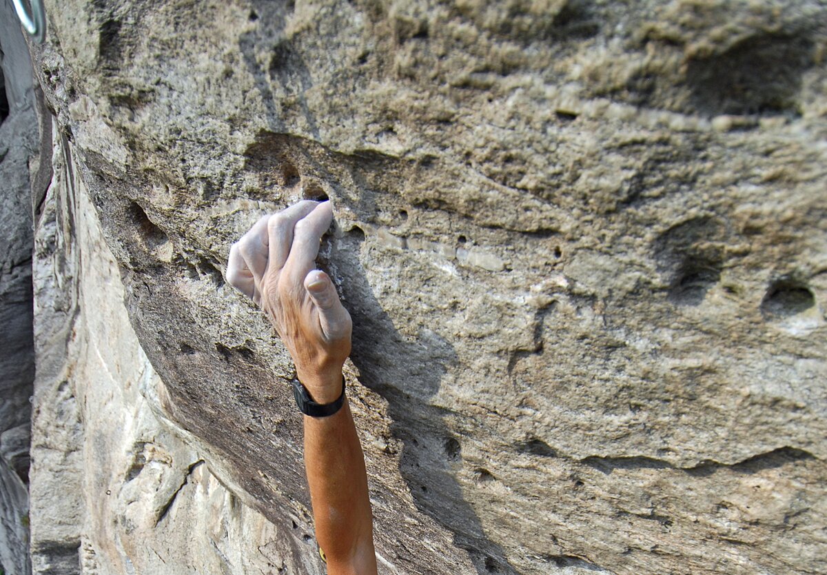 la mano di uno sportivo intento in una sessione di arrampicata su roccia: è bianca di magnesite