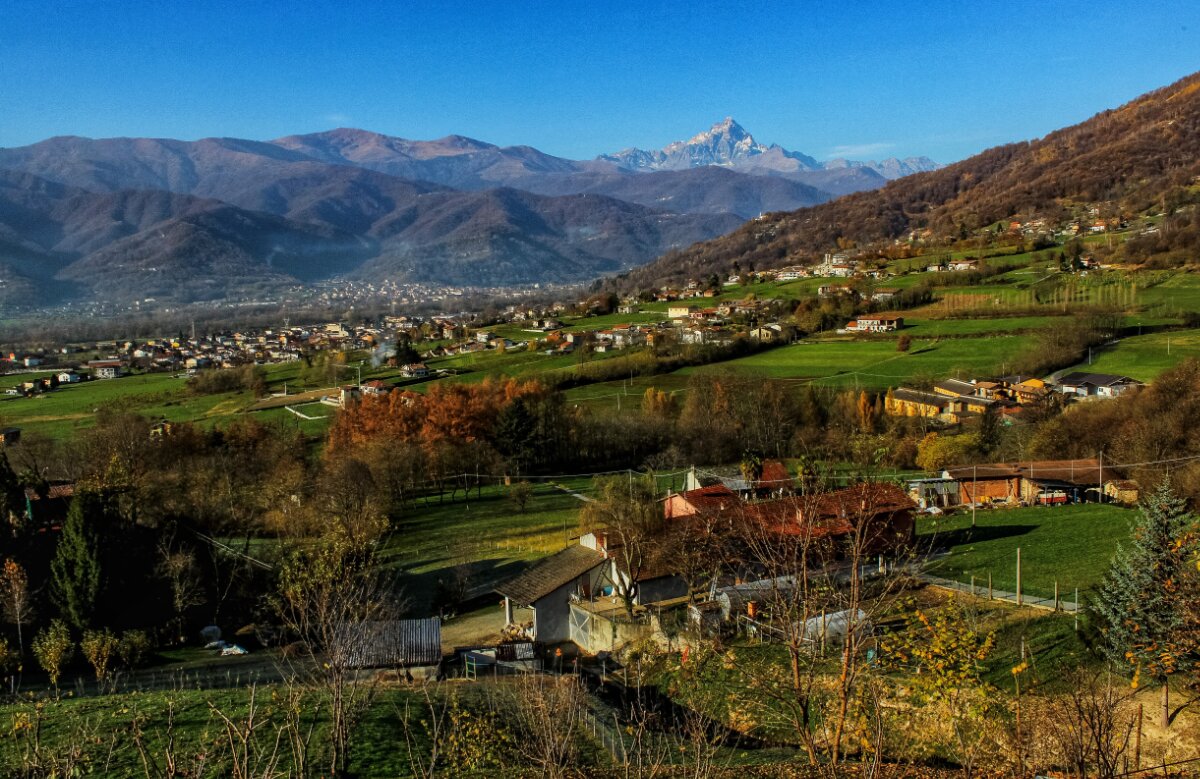 veduta autunnale del concentrico, circondato dalla vegetazione. sullo sfondo, in alto a destra, si staglia il Monviso