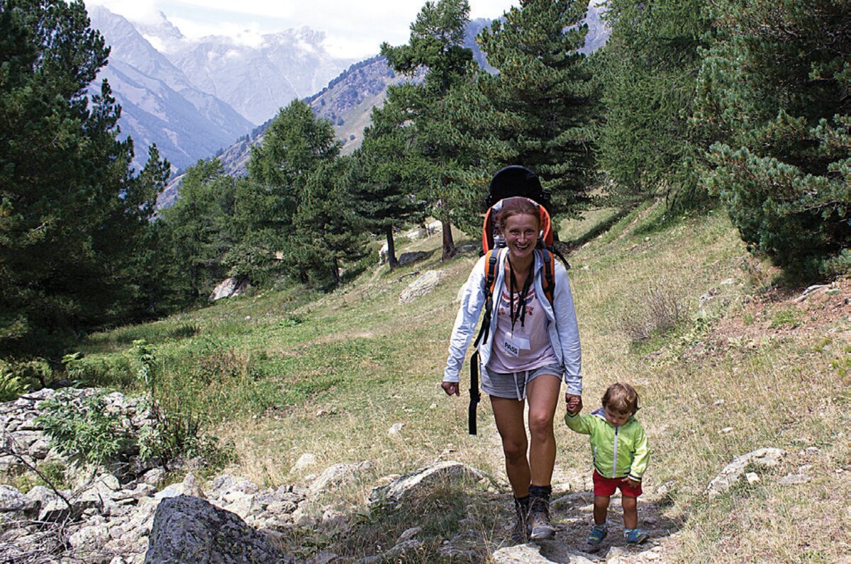 una giovane mamma tiene per mano una bimba lungo il sentiero; sullo sfondo alberi e un panorama verso l'alta valle Varaita