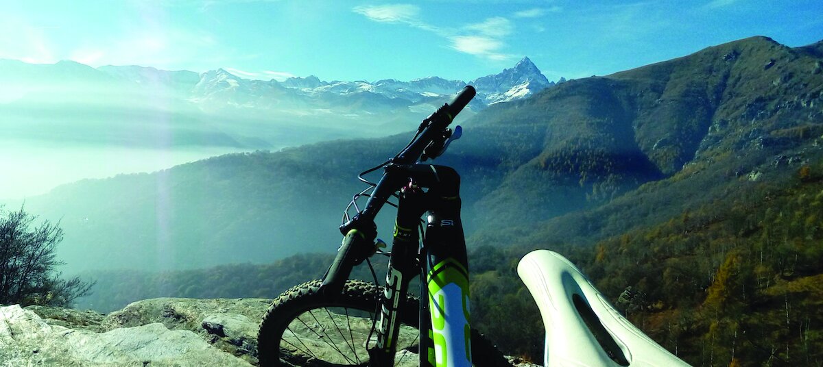 in primo piano il manubrio di una bicicletta MTB su un balcone panoramico che si affaccia sul Monviso