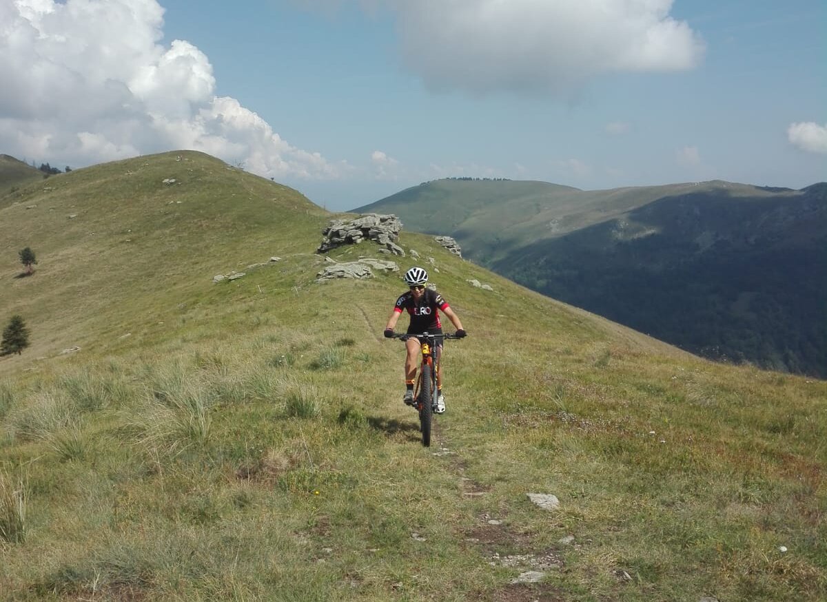 un ciclista percorre una sottile traccia sulla cresta di un rilievo, con fondo erboso.