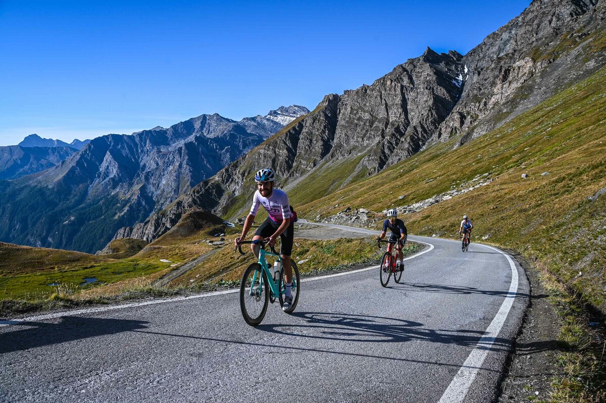 tre ciclisti risalgono la strada del Colle dell'Agnello in una giornata soleggiata e dal cielo terso. Non ci sono automobili sul percorso.