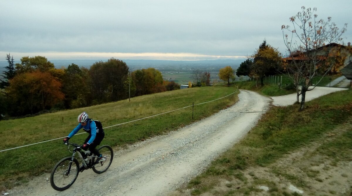 un ciclista in MTB sta percorrendo una strada bianca in territorio collinare, sullo sfondo dell'immagine si vede il fondovalle