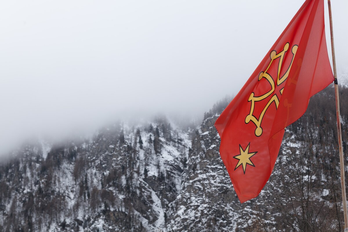 una bandiera occitana, rossa con croce di Tolosa gialla, in un panorama invernale