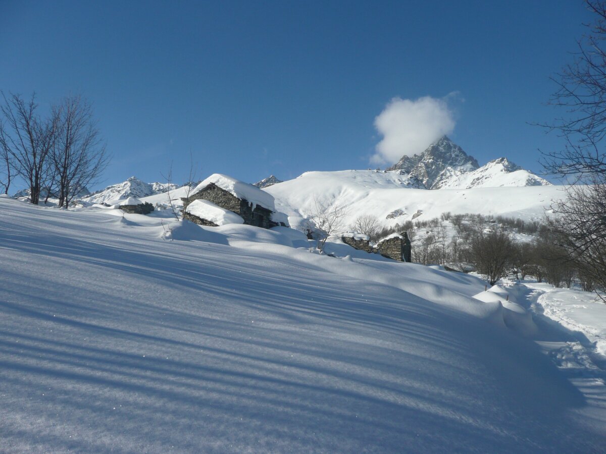 un borgo alpino immerso nella neve, con una traccia di sentiero sulla destra della foto. Sullo sfondo, il Monviso