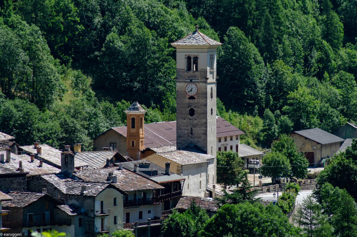 al centro della foto il campanile di Casteldelfino svetta sulle case circostanti. Intorno si vede una verde vegetazione estiva